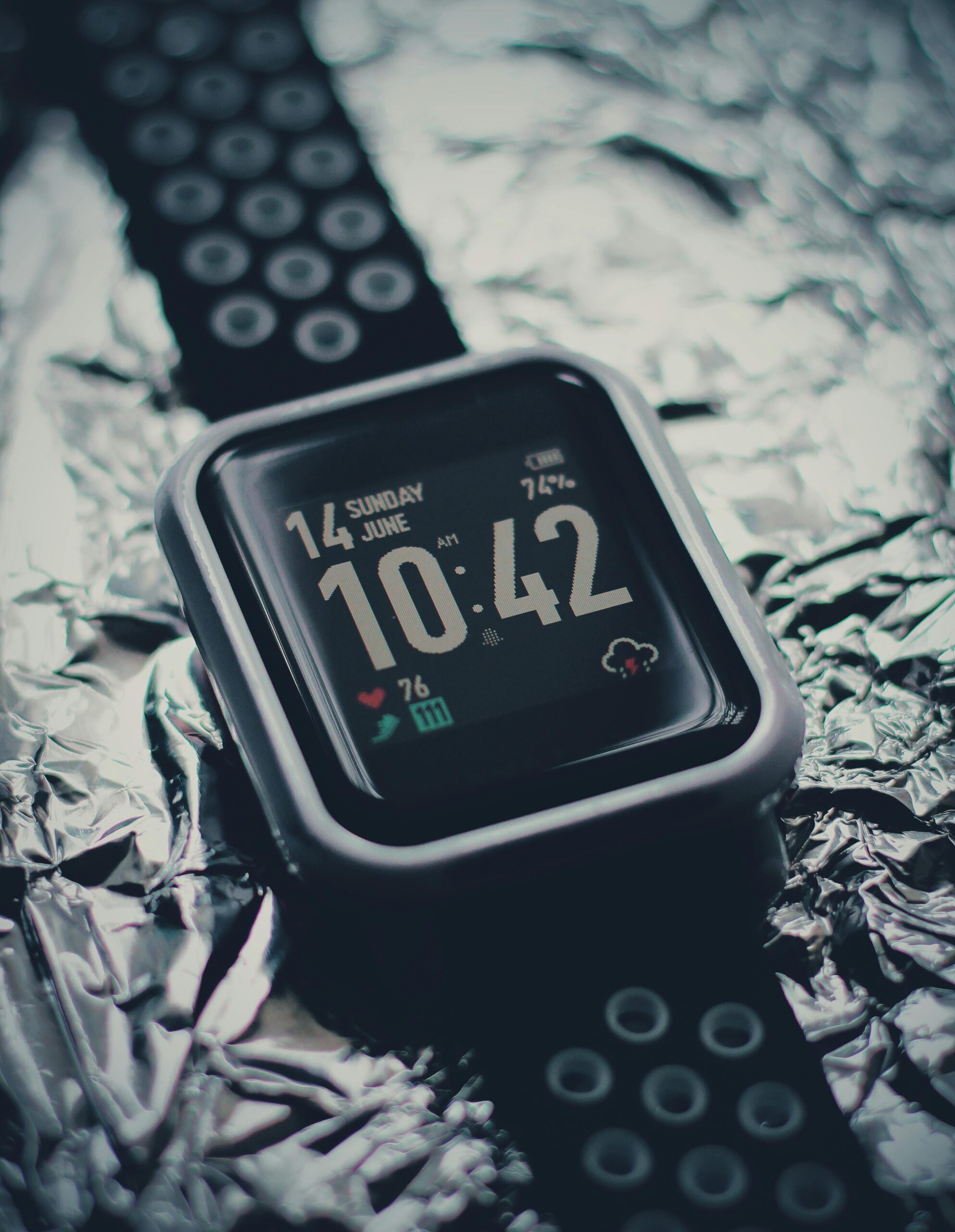 Stylish black smartwatch with digital display showing time and date on shiny foil background.